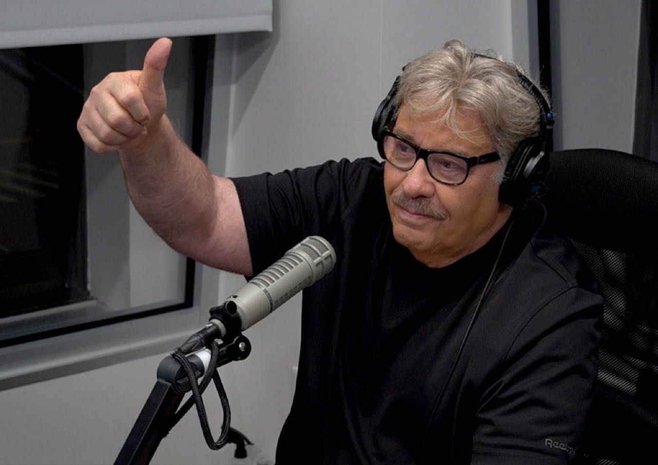 Tony Orlando giving a thumbs up while speaking into a microphone, wearing headphones in a recording studio.