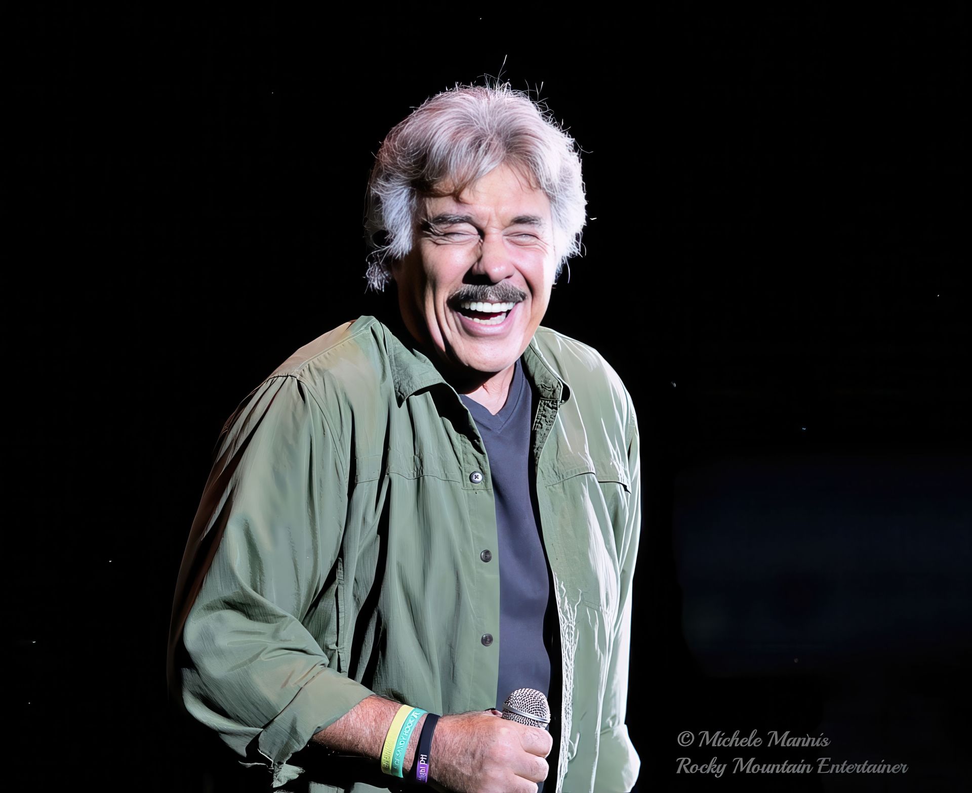 Tony Orlando smiling on stage while holding a microphone, dressed in a green jacket.