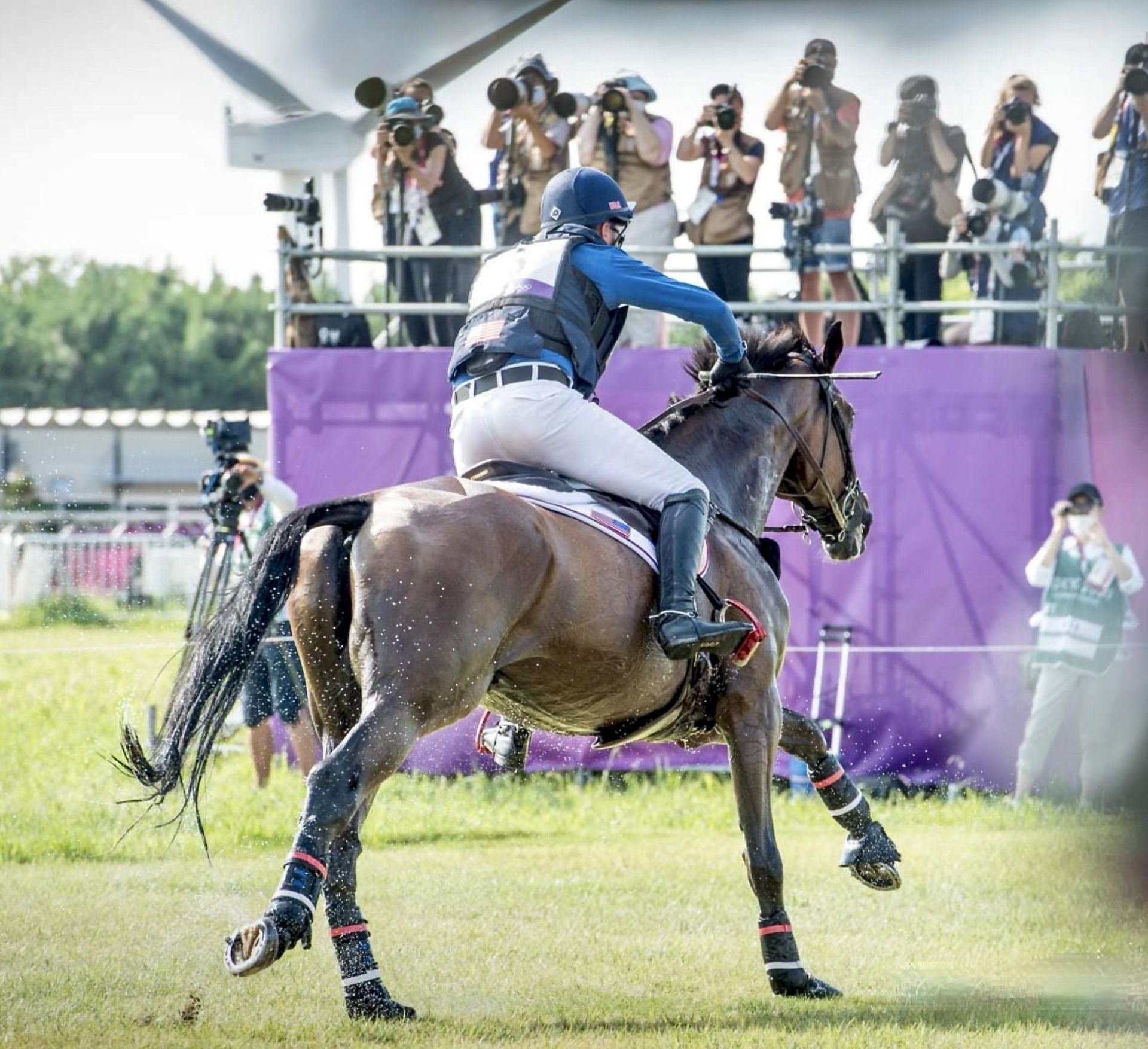 A rider competes on a horse during an event, with multiple photographers capturing the moment in the background.