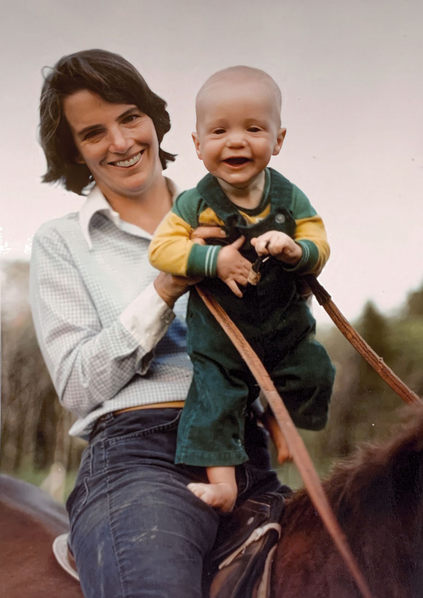 A smiling woman holding a baby while sitting on a horse, both appearing happy and enjoying the moment.