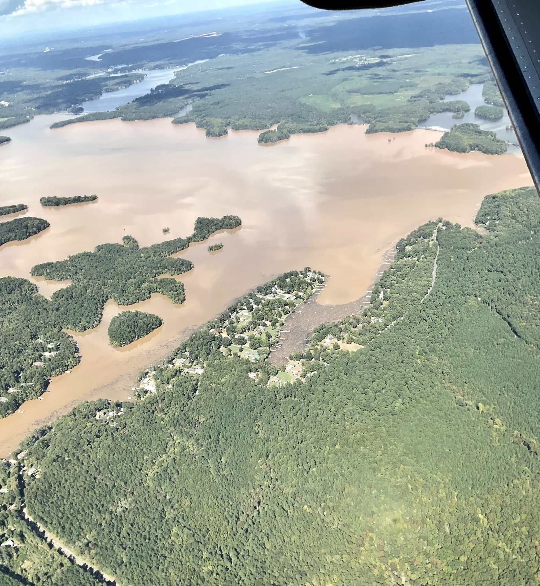 Aerial view of a landscape featuring a mix of muddy water and green islands, with patches of land appearing above the waterline, showcasing a rural area interspersed with trees and small settlements.