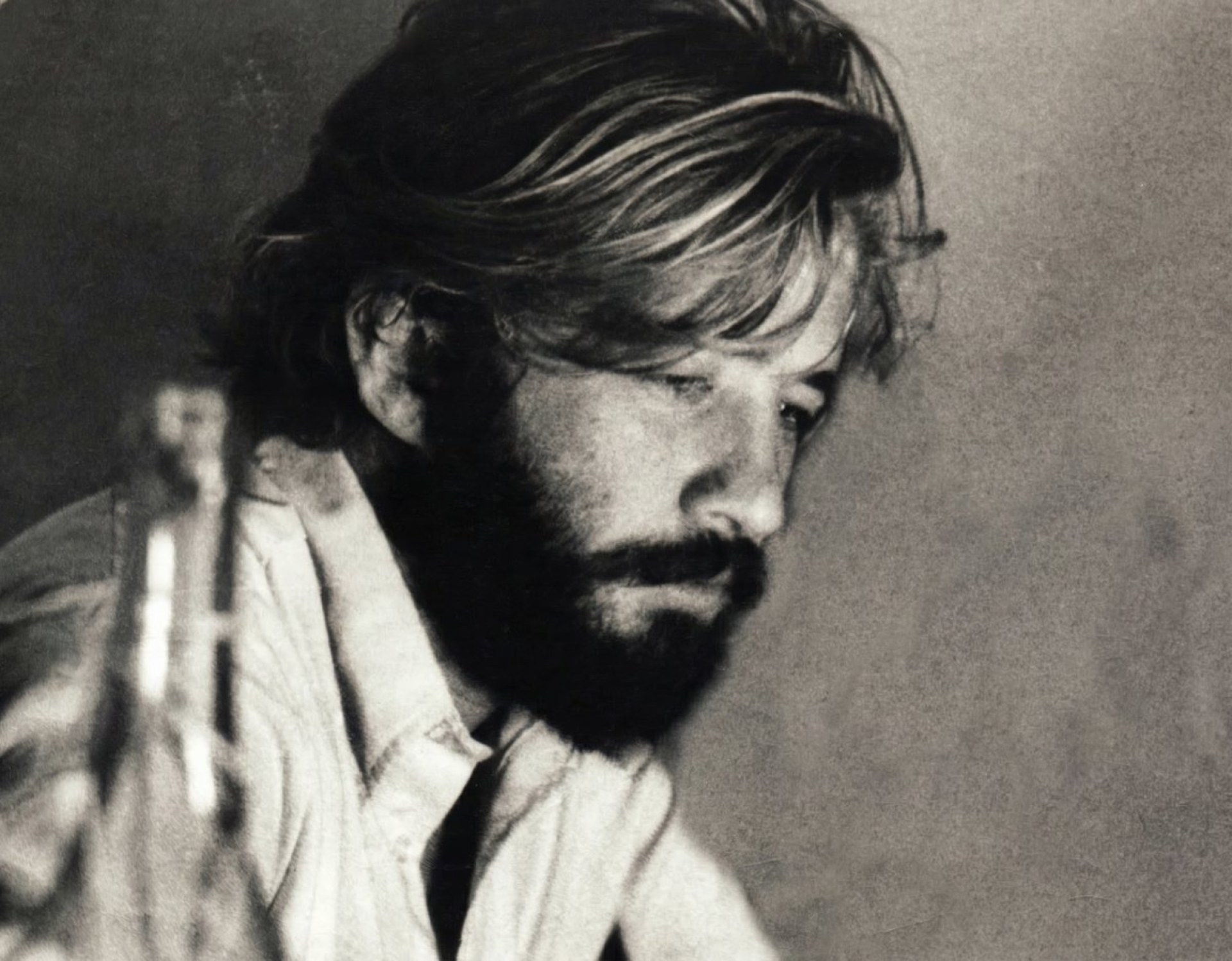 Black and white portrait of a contemplative man with long hair and a beard, looking downwards.