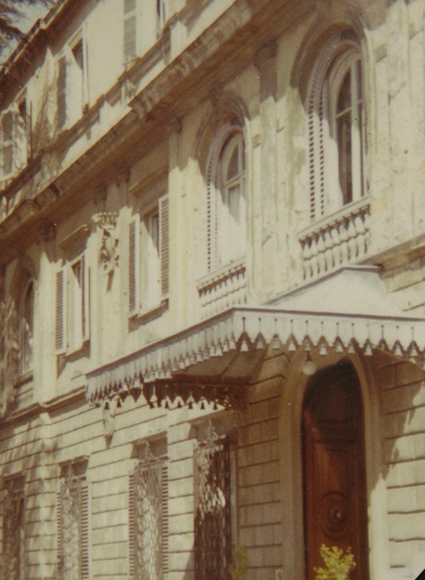 Facade of an old building featuring arched windows, decorative elements, and a porch with a canopy.