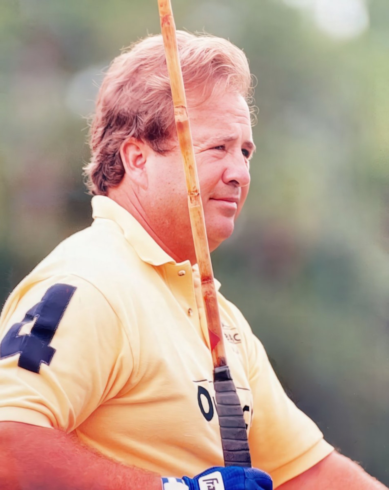 A man with short blonde hair wearing a yellow polo shirt with the number 4 on the sleeve, holding a golf club outdoors.
