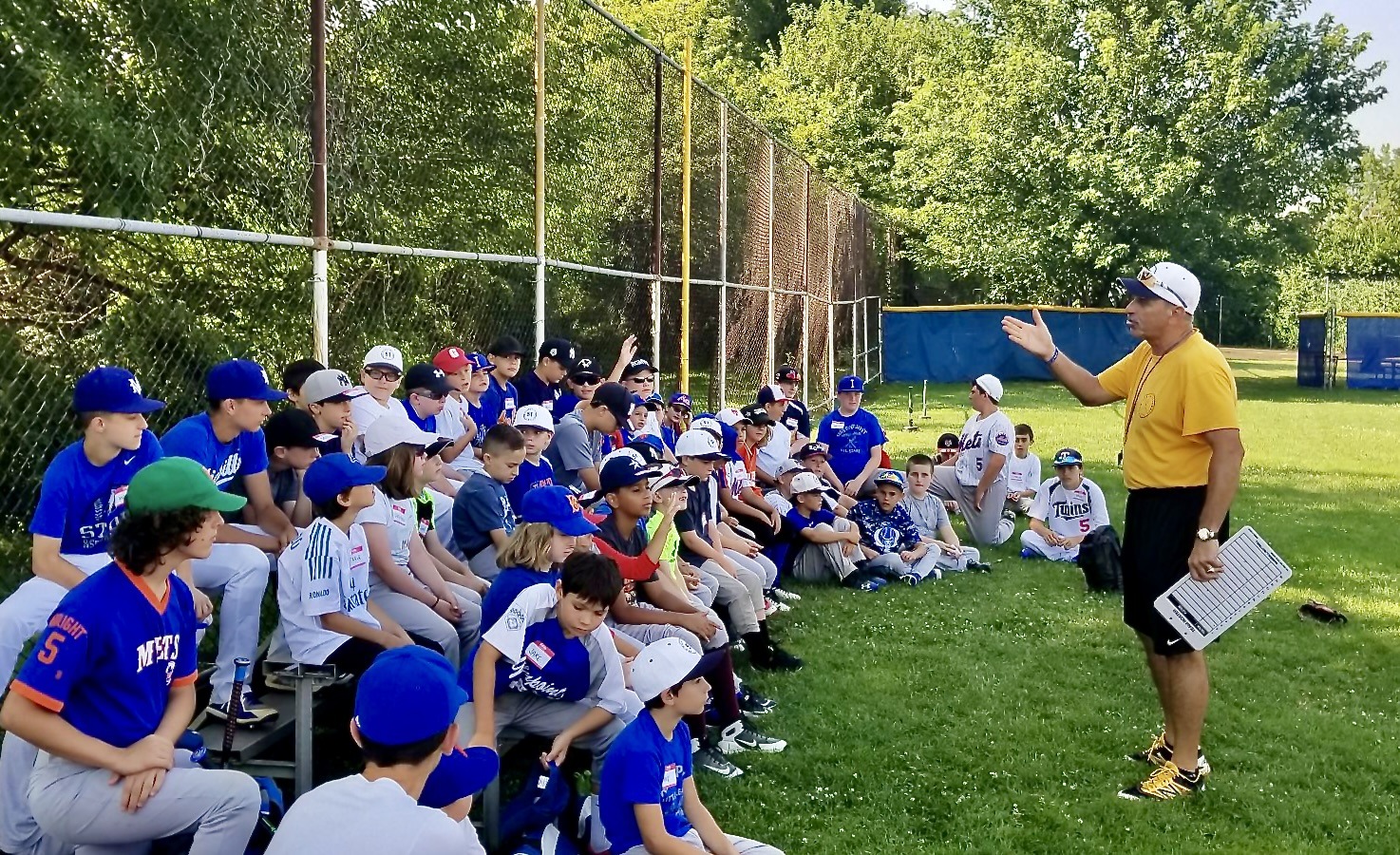 Dom Scala speaking to campers seated on the grass at his baseball camp